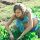 A young woman in a blue dress gardening outdoors surrounded by lush plants.